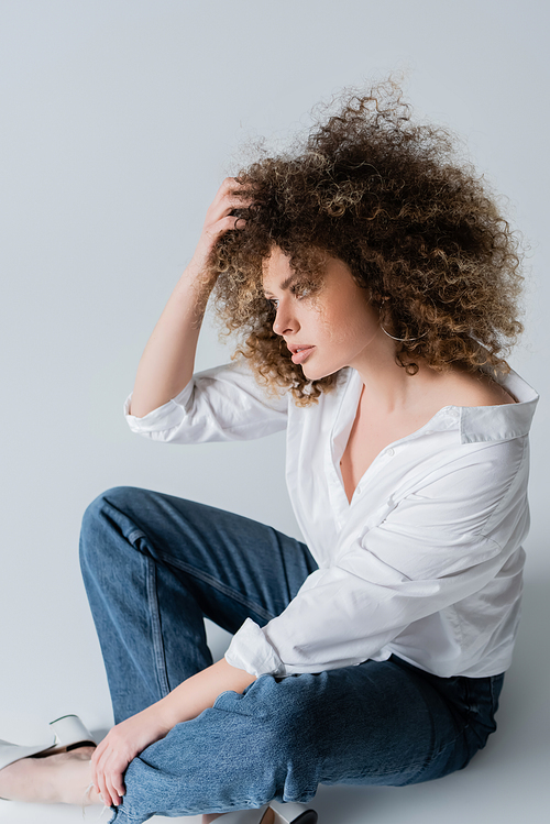 Pretty curly woman in blouse touching hair on white background