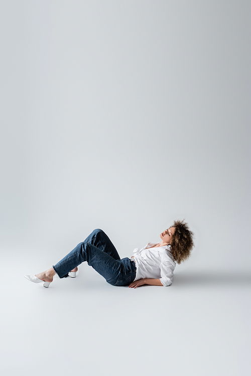 Curly woman in jeans lying on white background