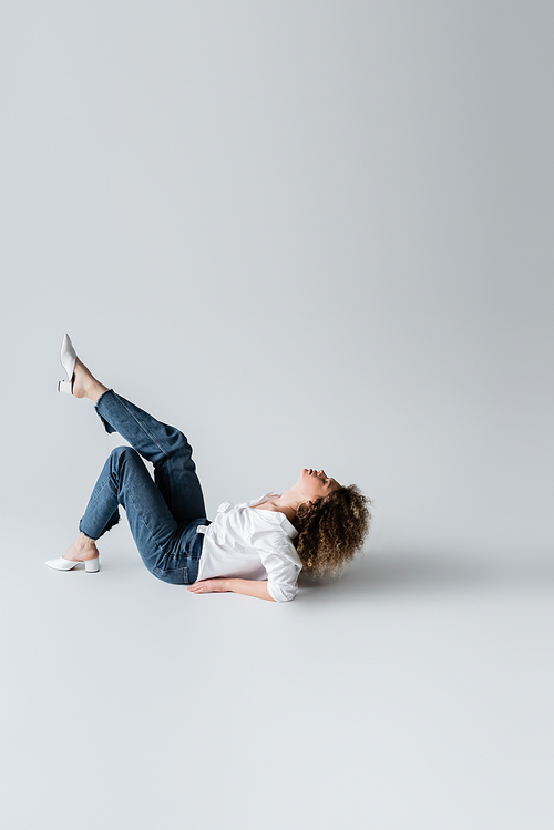 Side view of young curly woman lying on white background