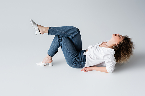 Stylish woman in jeans and blouse lying on white background