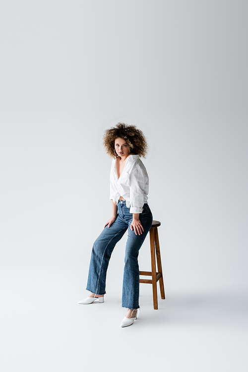 Stylish model in blouse posing near chair on white background