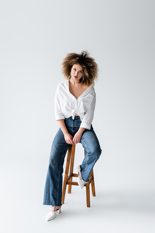 Curly model in blouse sitting on chair on white background