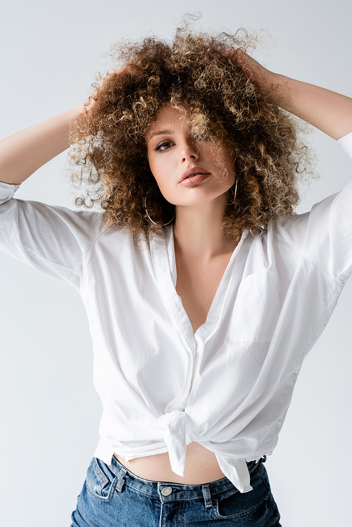 Curly young model in blouse touching hair isolated on white