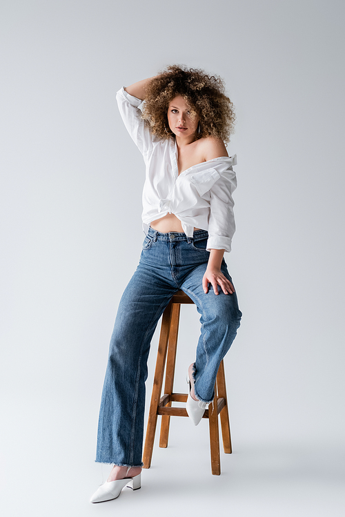 Trendy model in blouse sitting on chair on white background