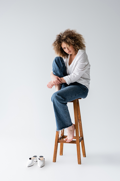 Pretty barefoot model sitting on chair on white background