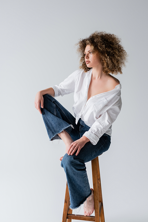 Young curly and barefoot model posing on chair isolated on white