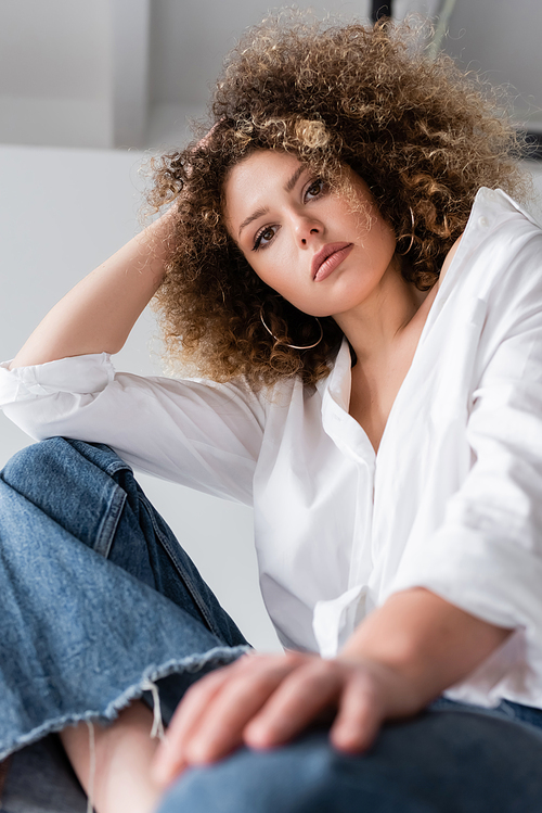 Low angle view of curly model in blouse looking at camera on white background