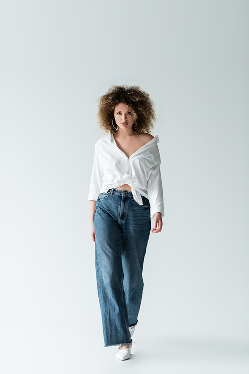 Curly woman in blouse walking on white background