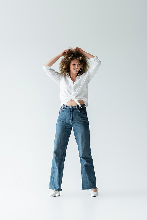 Smiling woman in blouse touching curly hair on white background