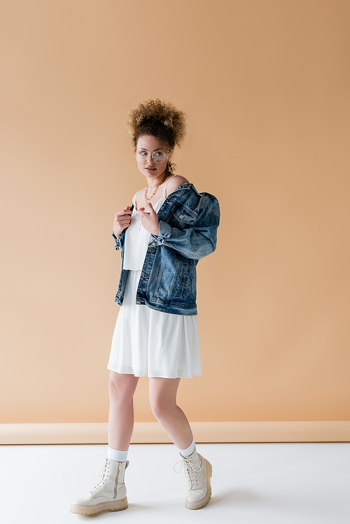 Trendy woman in eyeglasses and denim jacket on beige background