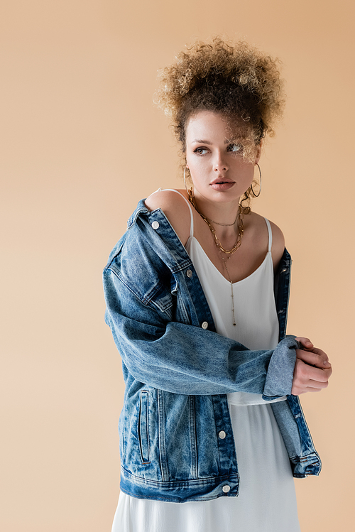 Curly woman in denim jacket looking away isolated on beige
