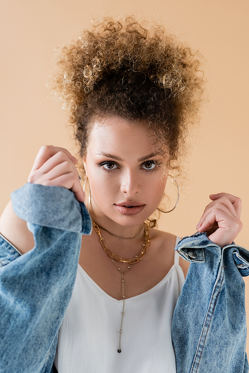 Portrait of stylish model in denim jacket looking at camera isolated on beige