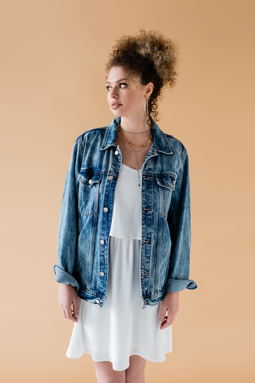 Smiling model in denim jacket looking away isolated on beige