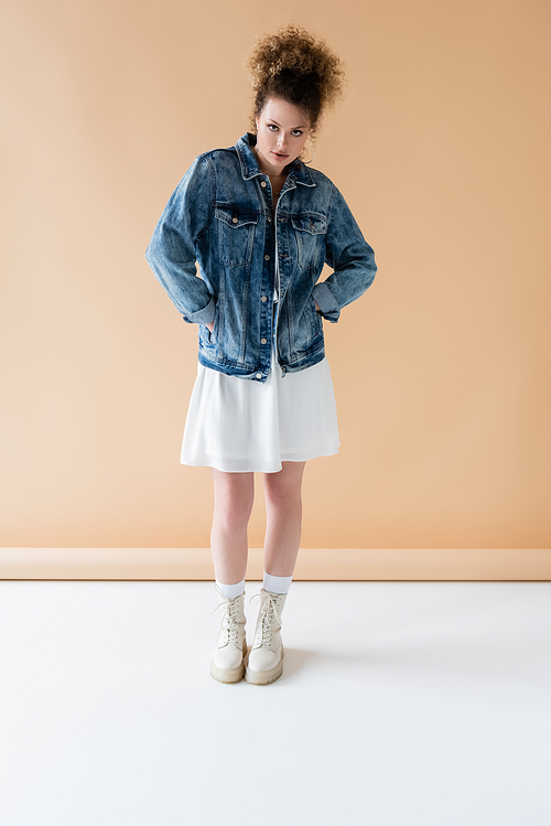 Full length of fashionable woman standing on beige background