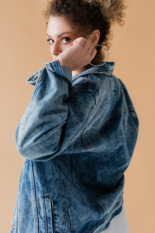 Curly woman in denim jacket looking at camera isolated on beige