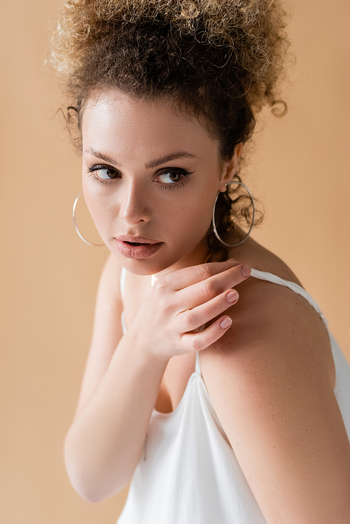 Curly model touching white top and looking away isolated on beige
