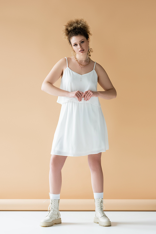 Full length of young woman in boots and white clothes on beige background
