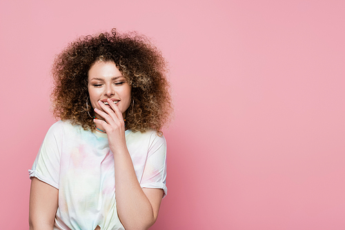 Positive curly woman touching lips isolated on pink