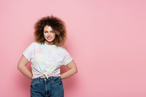 Smiling curly woman in t-shirt looking away on pink background