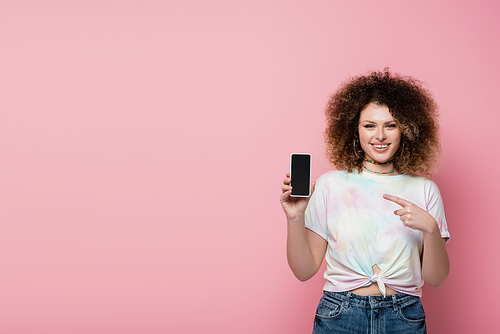 Cheerful woman pointing at mobile phone isolated on pink