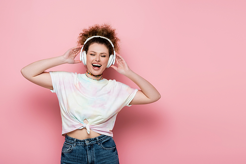 Positive woman in headphones singing on pink background