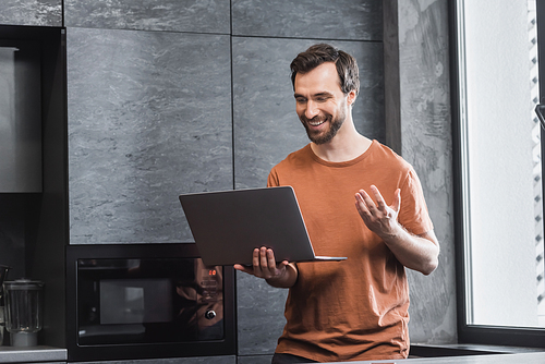 cheerful bearded man looking at laptop and gesturing during video call