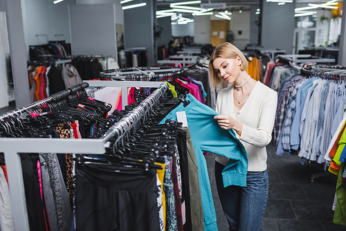 Young blonde woman choosing pants in second hand