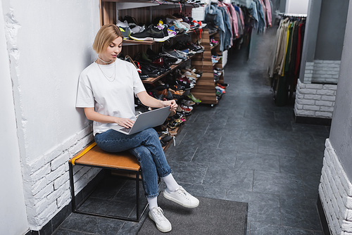 Blonde retailer using laptop near shoes in vintage shop