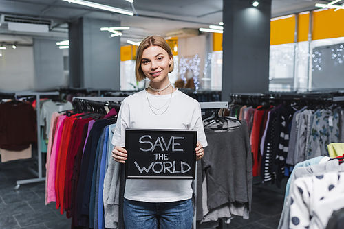Smiling saleswoman holding board with save the world lettering in second hand