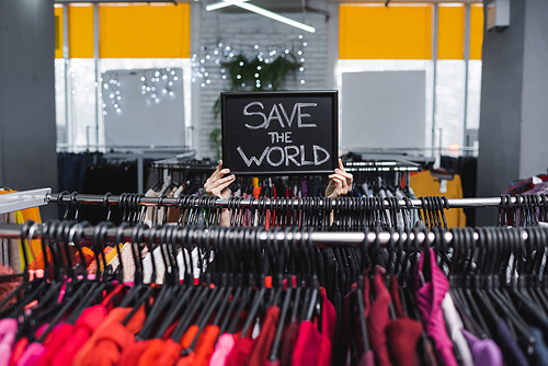Cropped view of retailer holding board with save the world lettering near clothes in second hand