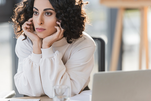 Muslim businesswoman looking away near blurred laptop in office