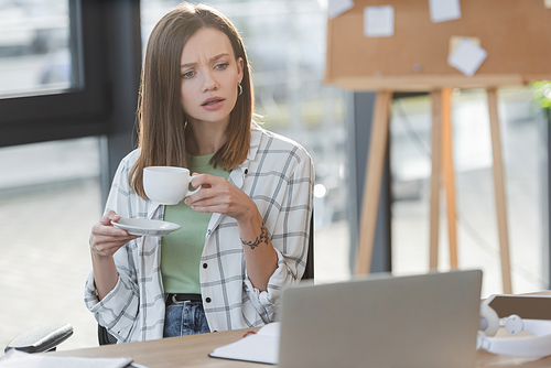 Focused businesswoman holding cup near laptop in office