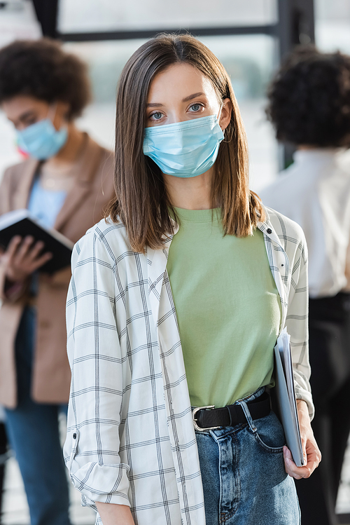 Young businesswoman in medical mask holding paper folder in office