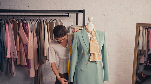 Designer measuring elegant jacket on mannequin in atelier