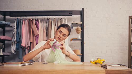 Designer in eyeglasses making dress on small mannequin in atelier