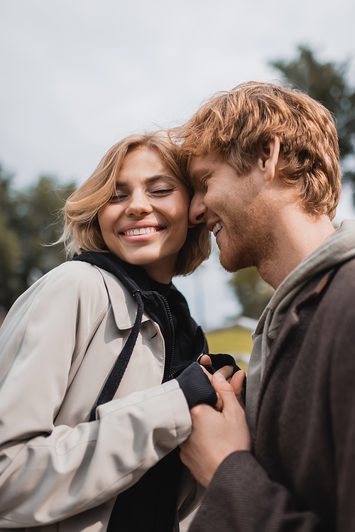 happy redhead man and blonde woman smiling while holding hands outdoors