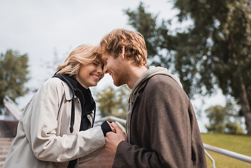 happy redhead man and cheerful woman smiling while holding hands outdoors