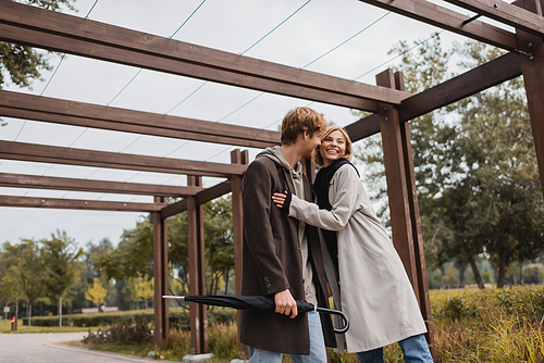 smiling young couple in autumnal coats hugging under multiple arch in park