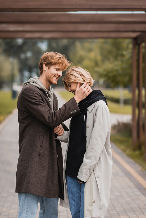 happy young man in autumnal coat hugging woman under arch in park