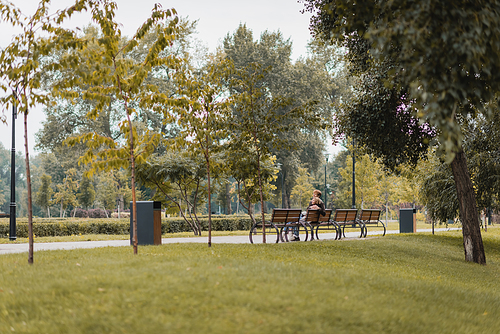 happy young man and woman sitting on wooden bench in green park