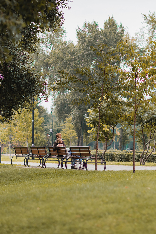 happy young man and woman hugging and sitting on wooden bench in green park