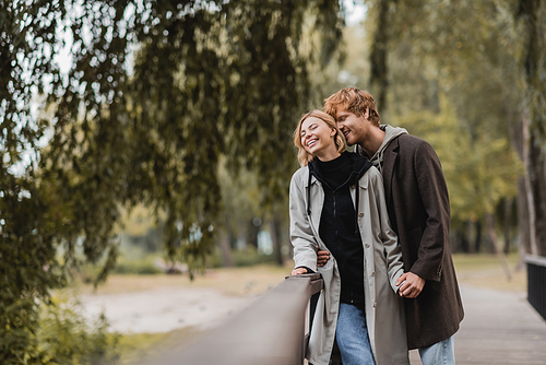 redhead man and blonde woman in coat smiling during date in park