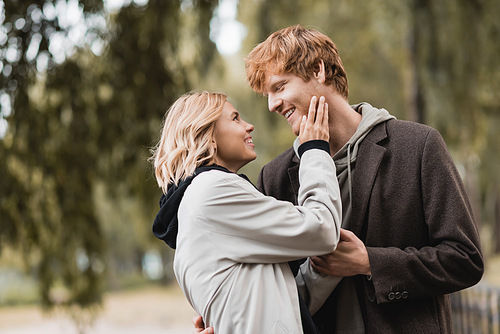 redhead man and blonde woman in coat smiling while having date in park