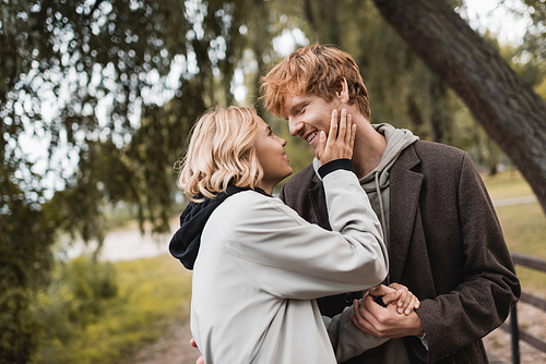 cheerful redhead man and blonde woman in coat smiling during date in park