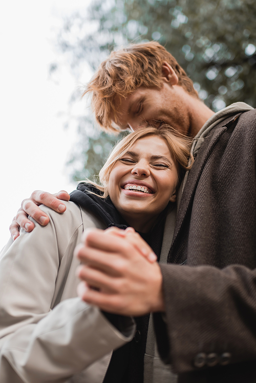 low angle view of redhead man kissing head of happy blonde woman during date in park