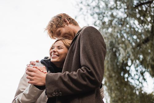 low angle view of redhead man kissing head of cheerful blonde woman during date in park