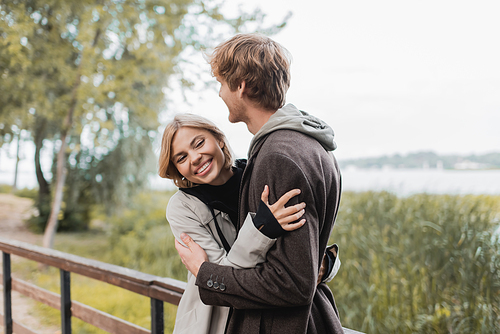 blonde woman smiling and hugging redhead man during date on bridge