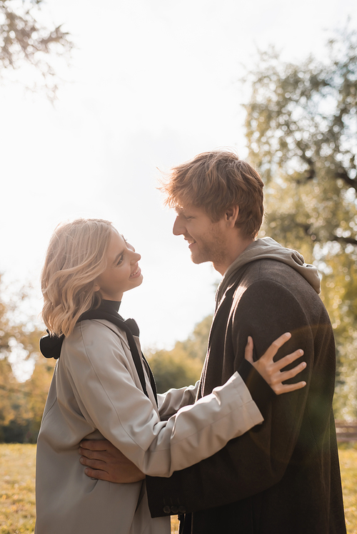 side view of young and joyful couple smiling while hugging in autumnal park