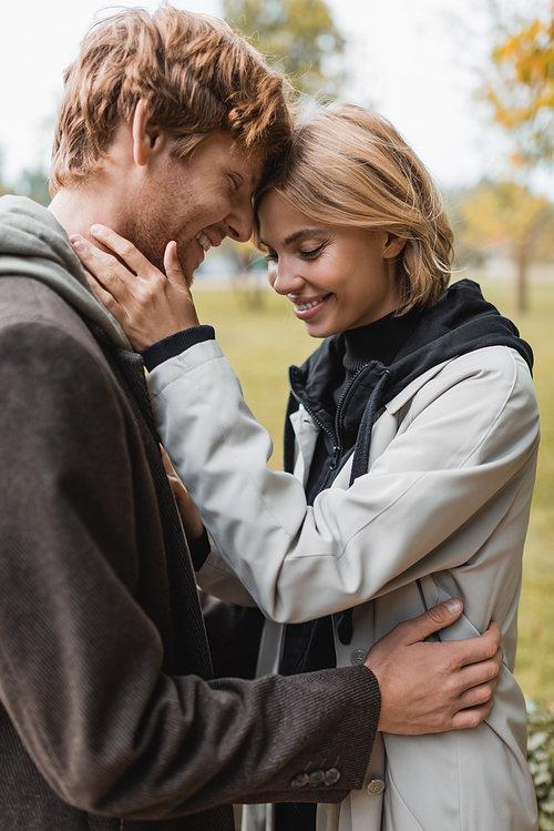 joyful young couple with closed eyes embracing in autumnal park during date