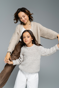 cheerful brunette woman dancing with daughter looking at camera isolated on grey